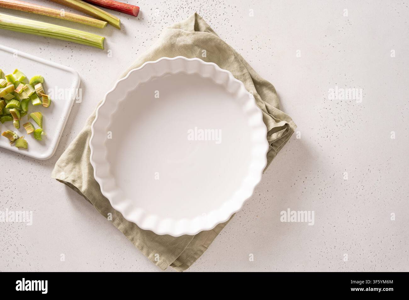 Empty ceramic pie dish with fresh rhubarb ingredients on white kitchen background Stock Photo