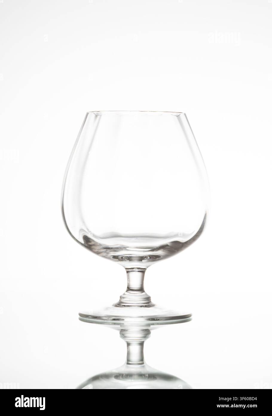Clear empty brandy glass sitting on a reflective white background Stock Photo
