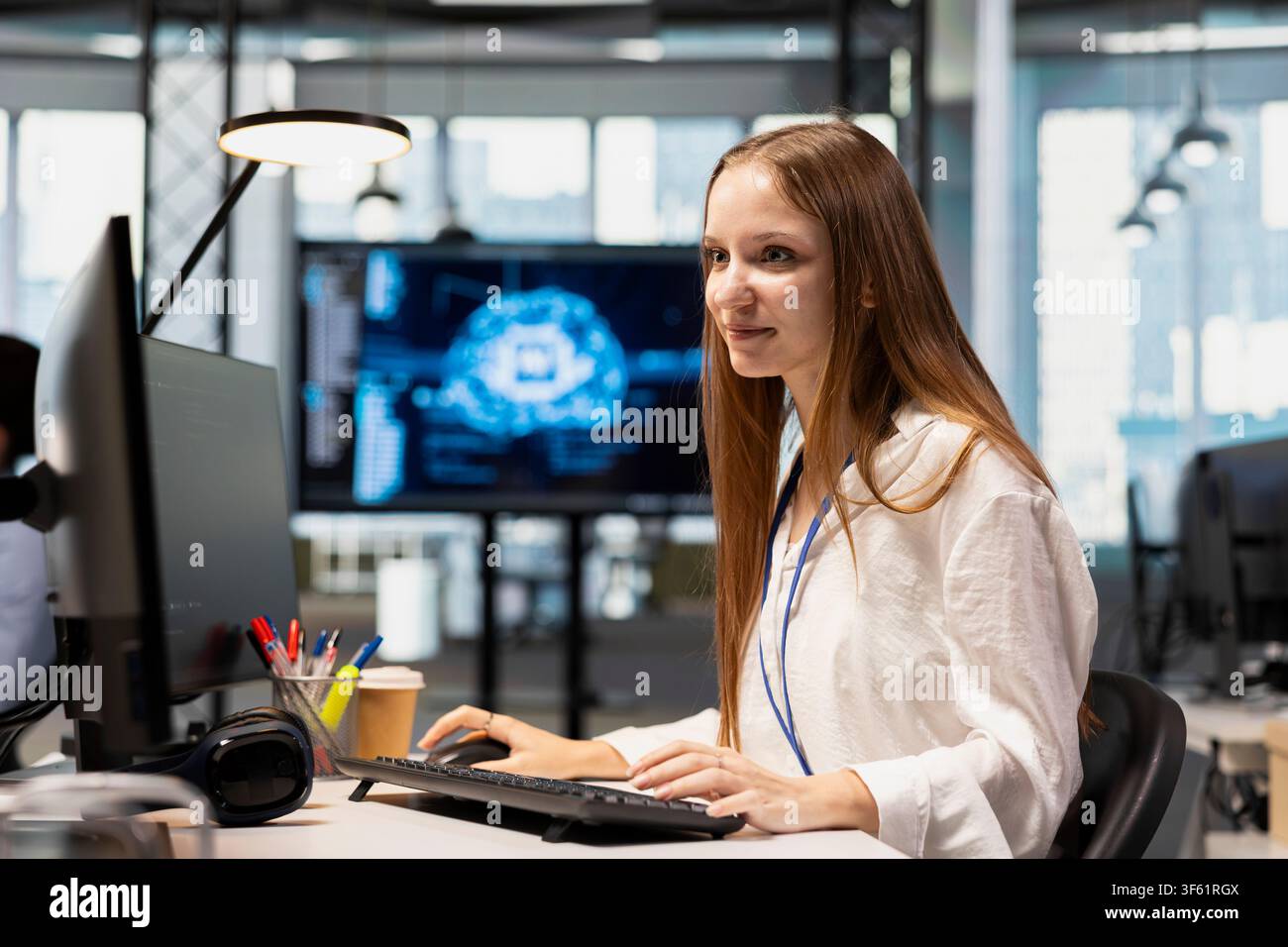 Cheerful junior dev in office using AI on computer to streamline app development. Joyous IT department intern at desk using PC to run debugging programs with machine learning technology Stock Photo