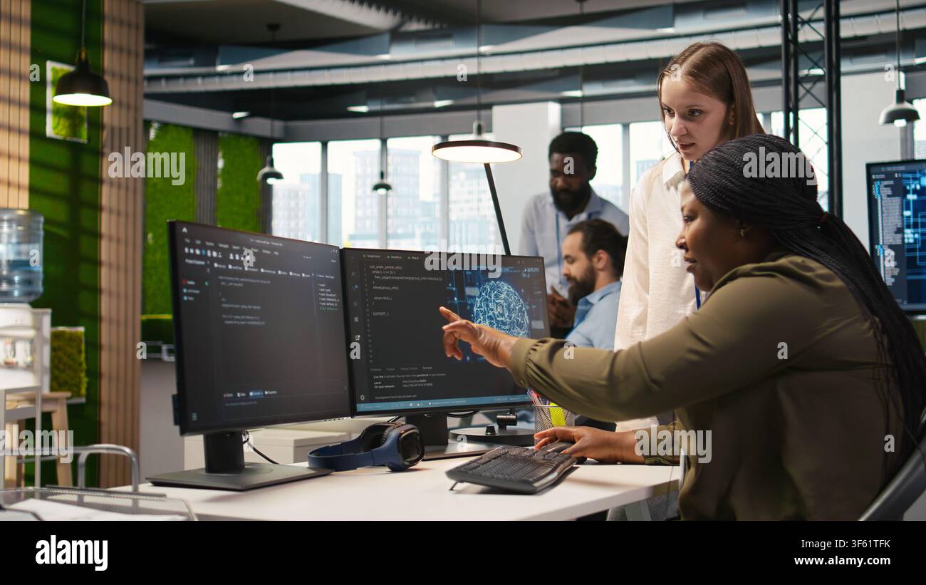Manager teaching young technician how to develop software and optimize code using AI. Team leader guiding intern in office on how to use artificial intelligence to resolve bottlenecks, camera A Stock Photo