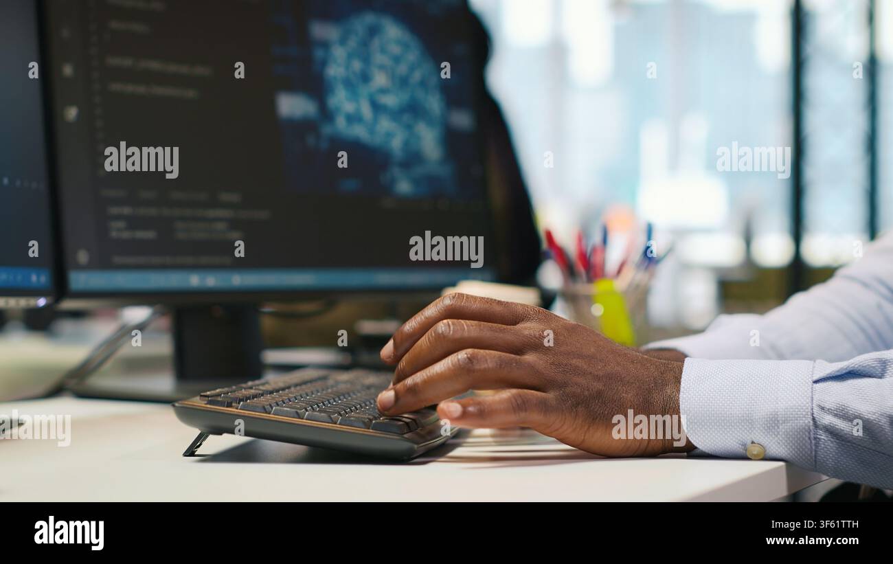 System administrator at office desk developing software applications using AI automation. IT specialist working on computer, debugging applications with artificial intelligence, camera A Stock Photo