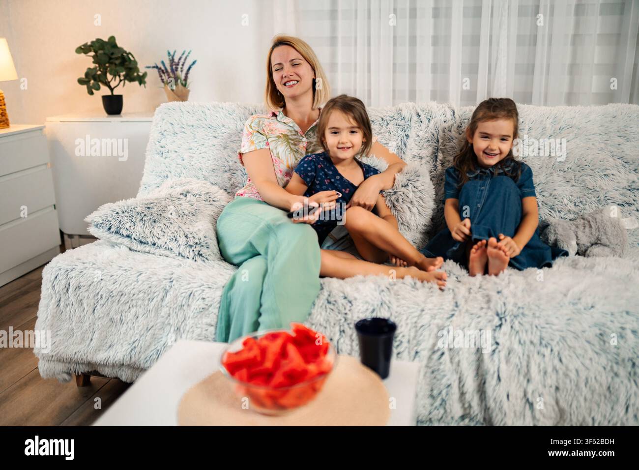 Mother and daughters relaxing on sofa watching TV at home Stock Photo