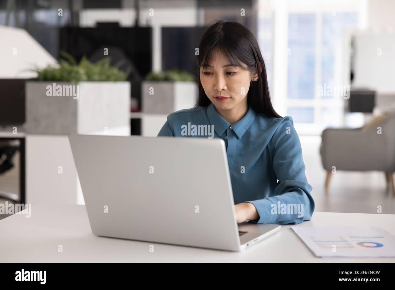 Serious Asian woman working on laptop in office Stock Photo