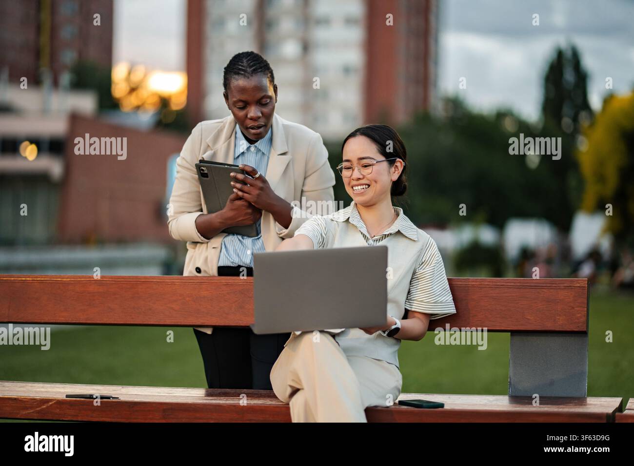 Two diverse businesswomen collaborating on a project using technology outdoors Stock Photo