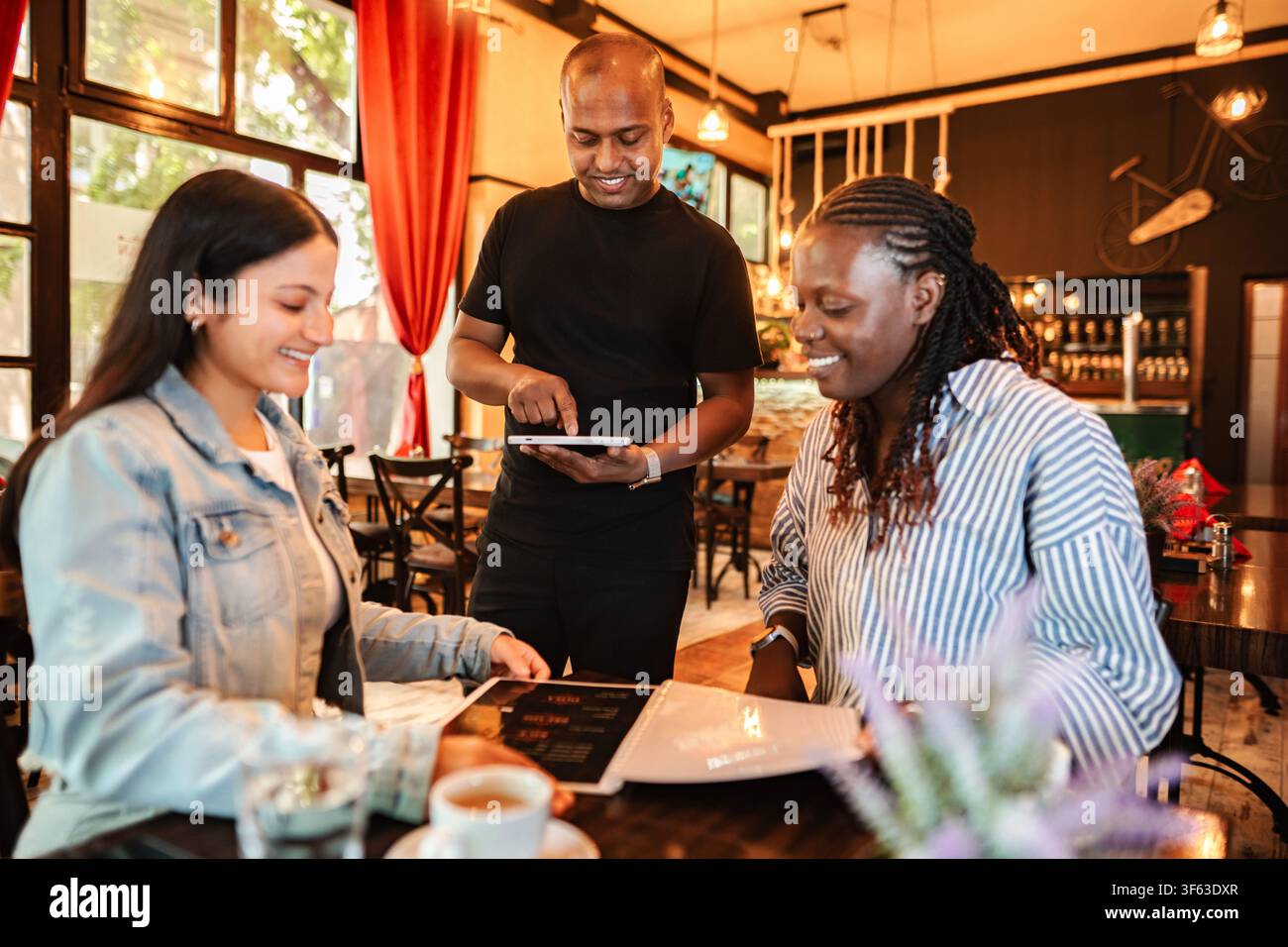 Waiter taking order from diverse women using a digital menu Stock Photo