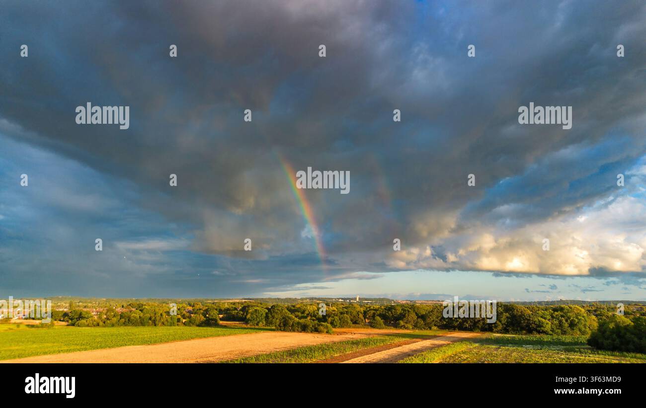 Brooding dark clouds and rainbow over fields in Cheshire. Stock Photo