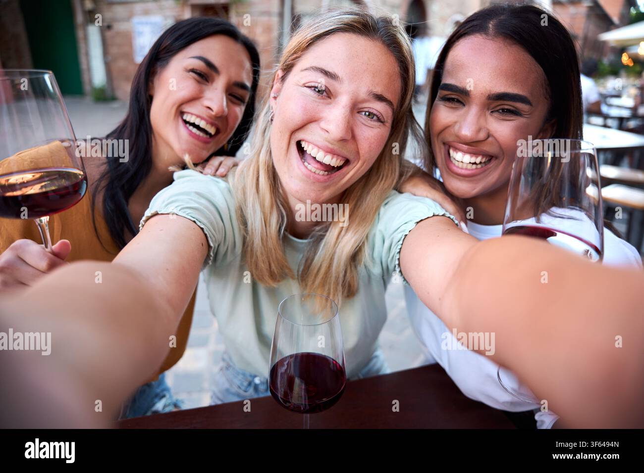 Three happy multi-ethnic friends taking selfie while drinking wine in a restaurant Stock Photo