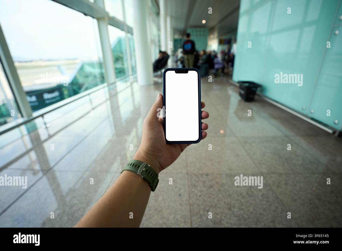 Hand holding smartphone with blank screen at airport. Stock Photo