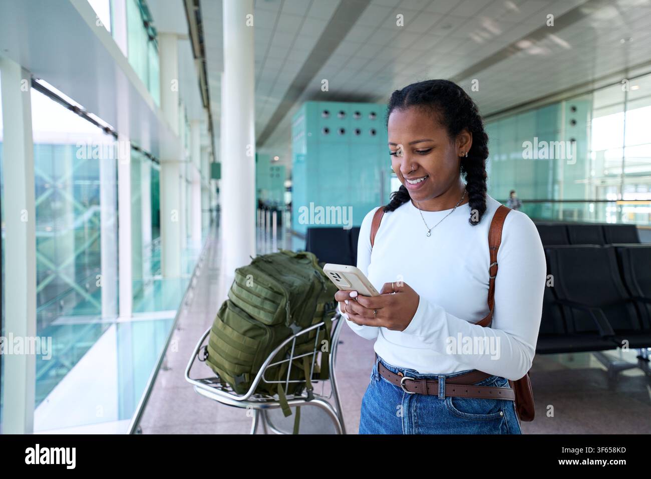 Young woman smiling, using smartphone in airport terminal. Stock Photo