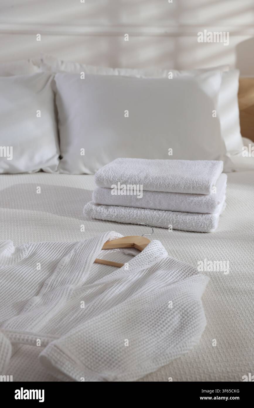 Clean bathrobe and towels on bed indoors Stock Photo
