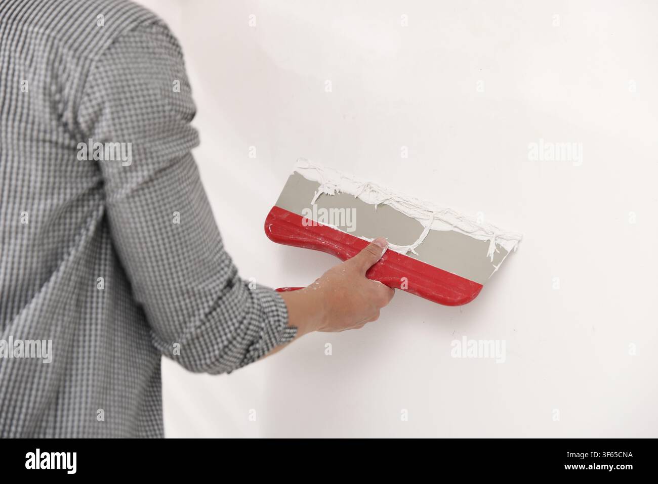 Worker plastering white wall with putty knife indoors, closeup Stock Photo