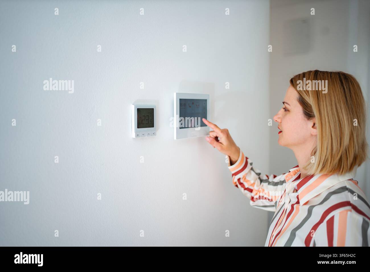 Woman adjusting smart home thermostat control panel Stock Photo
