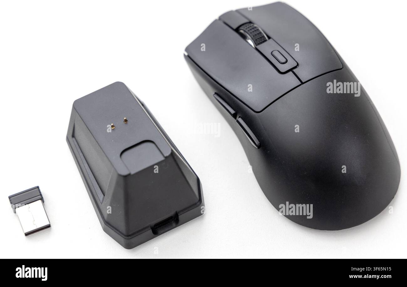 A wireless computer mouse is displayed next to its charging dock and a USB receiver on a white surface Stock Photo