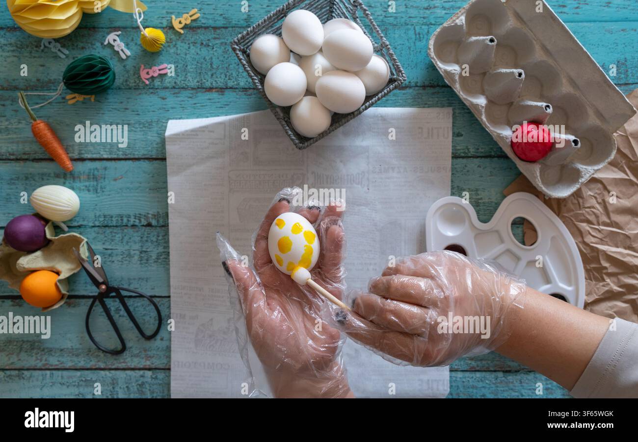 Human hands decorating Easter eggs with colorful dye surrounded by festive Easter decorations on a tabletop Stock Photo