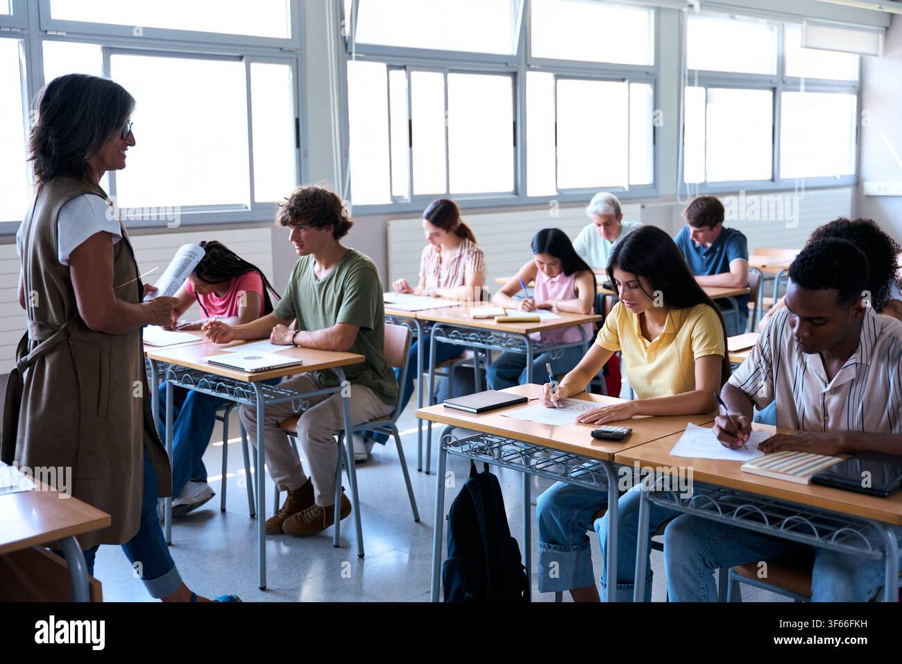 Students taking exam while teacher supervises in classroom Stock Photo