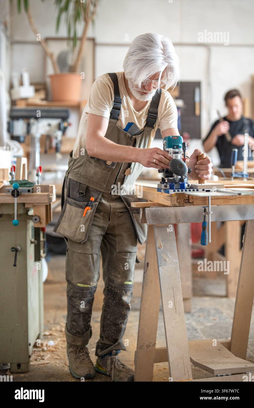 Carpenter works with handheld electric router machine on rail with additional stabilization handle. Stock Photo