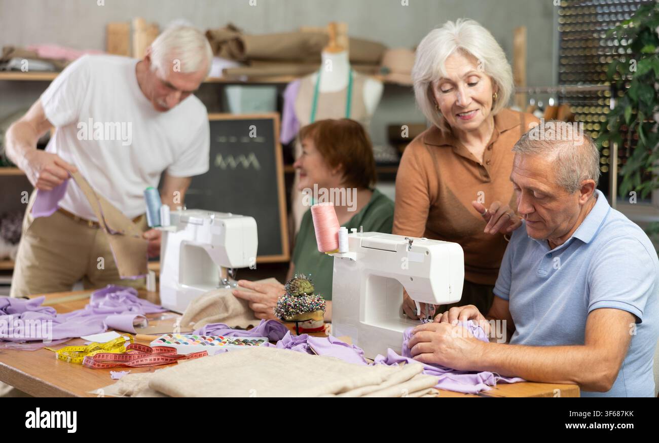 Some people communicate and discuss pattern, while others sew using sewing machine at lesson Stock Photo