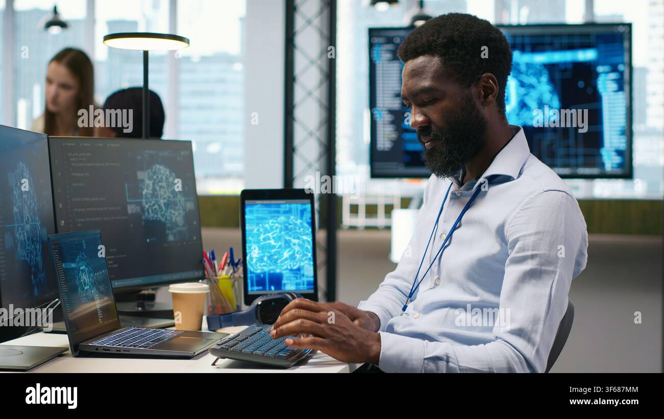 System administrator at office desk developing software using AI, listening music. IT expert wearing audio headset working on computer, debugging applications with artificial intelligence, camera A Stock Photo