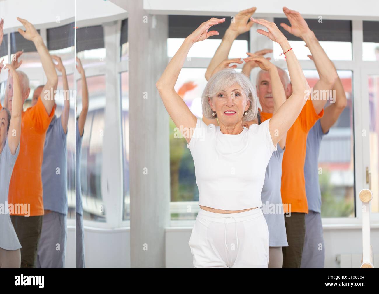 Active mature woman practicing fifth position holding by ballet barre together with others Stock Photo