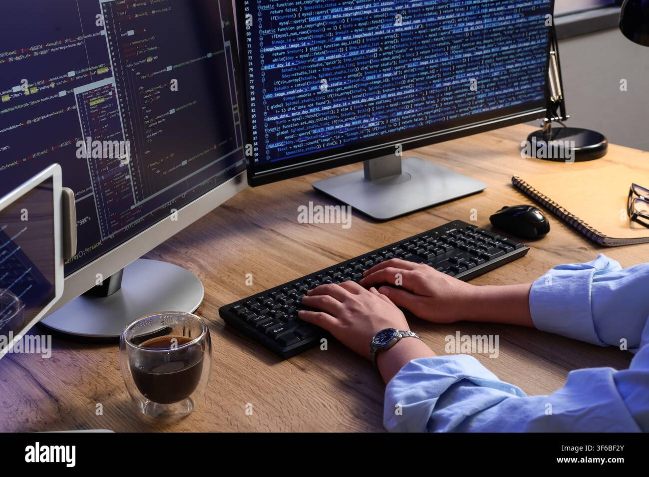 Programmer hands typing on a keyboard with multiple computer screens displaying code software development and IT, this setup software development info Stock Photo