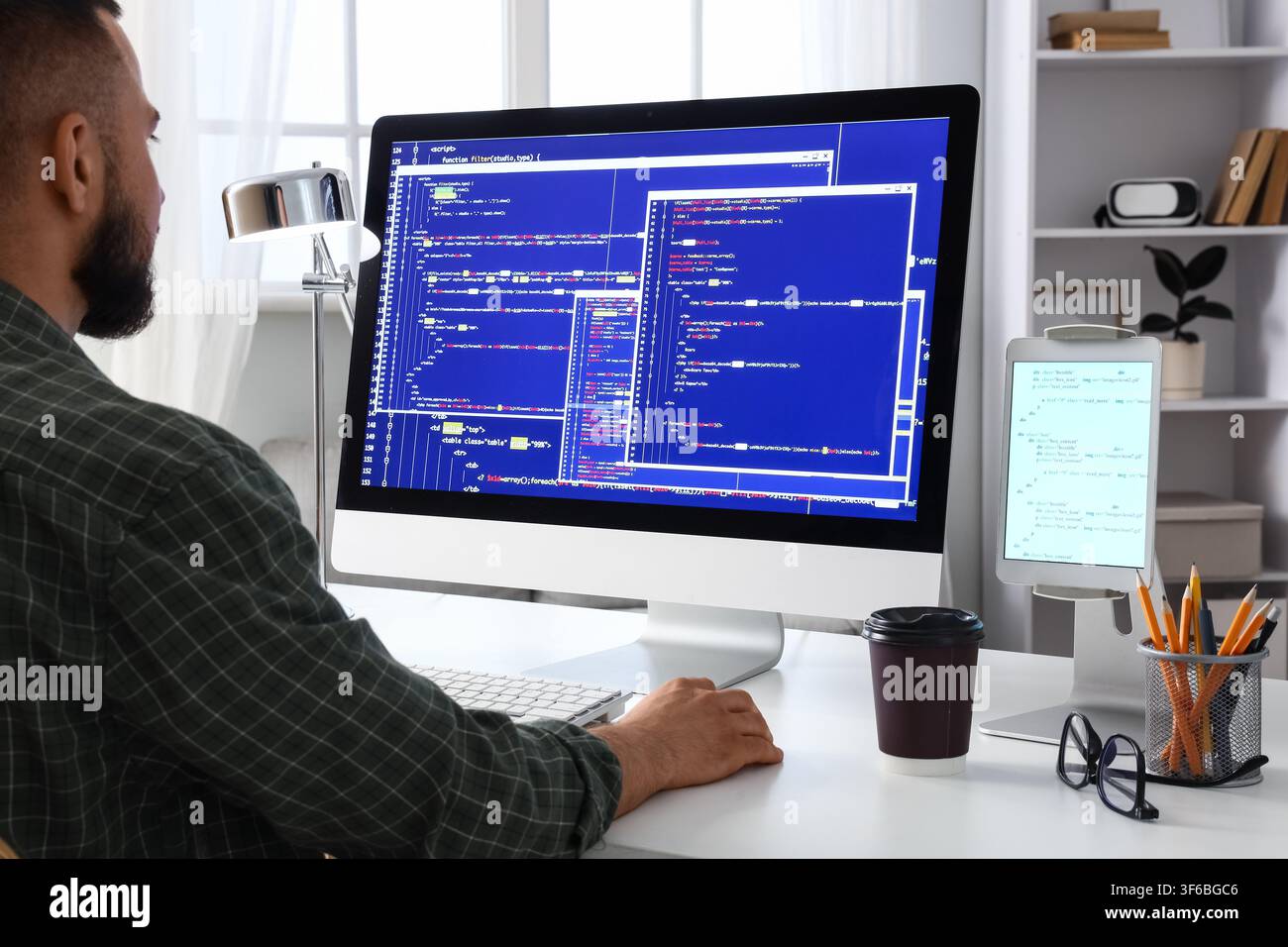 Male programmer coding on a desktop computer with multiple windows of script and data, software development Stock Photo