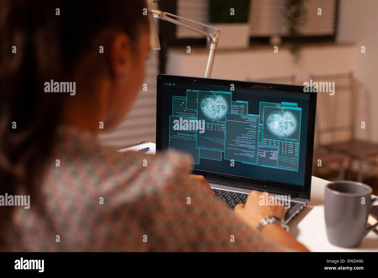 Female hacker uses a home laptop to attack a protected firewall while developing malicious code during the night. Stock Photo