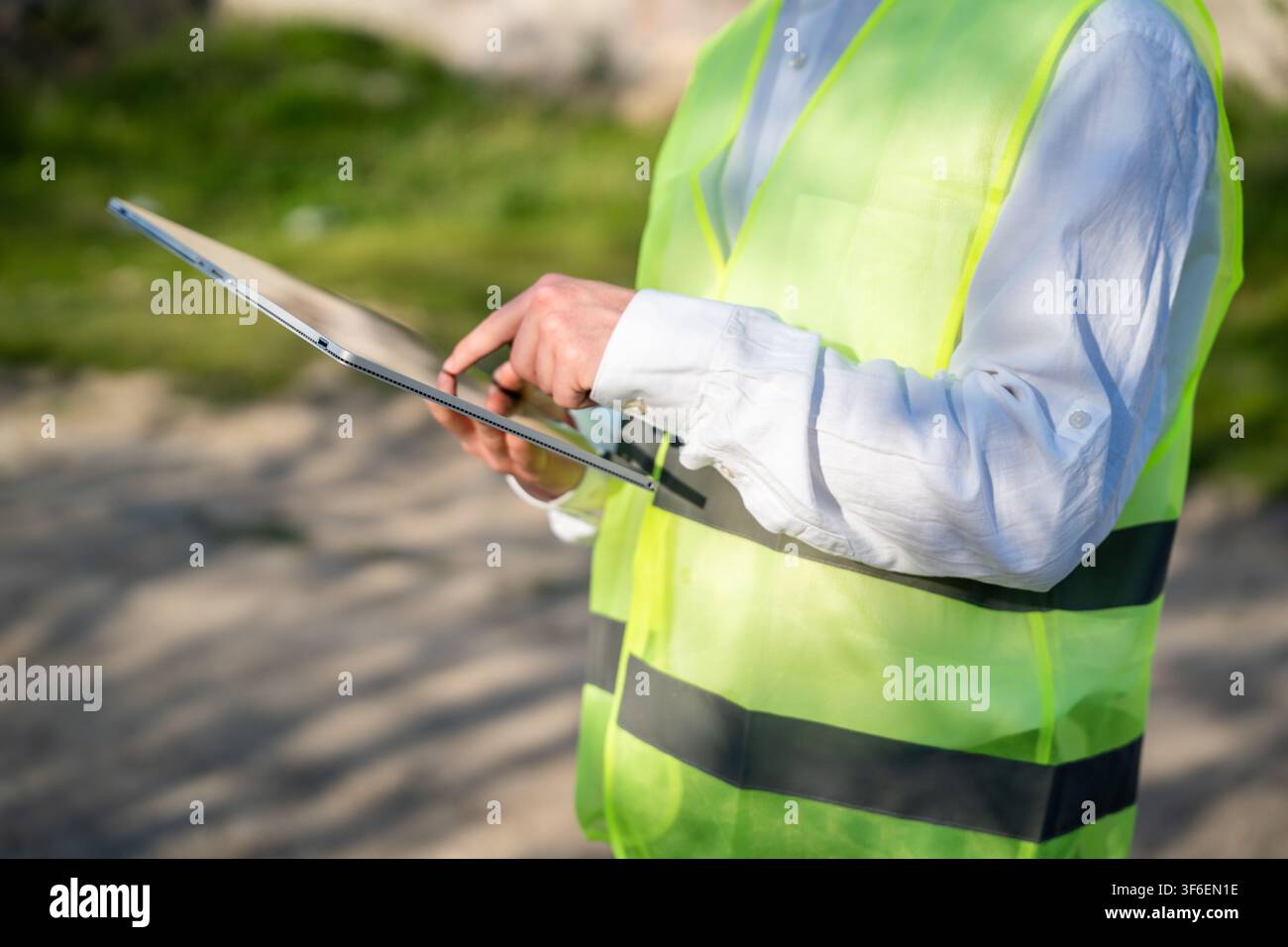 Engineer using tablet computer on construction site wearing safety vest. Digital workflow mobile construction documentation and engineering tools. Stock Photo