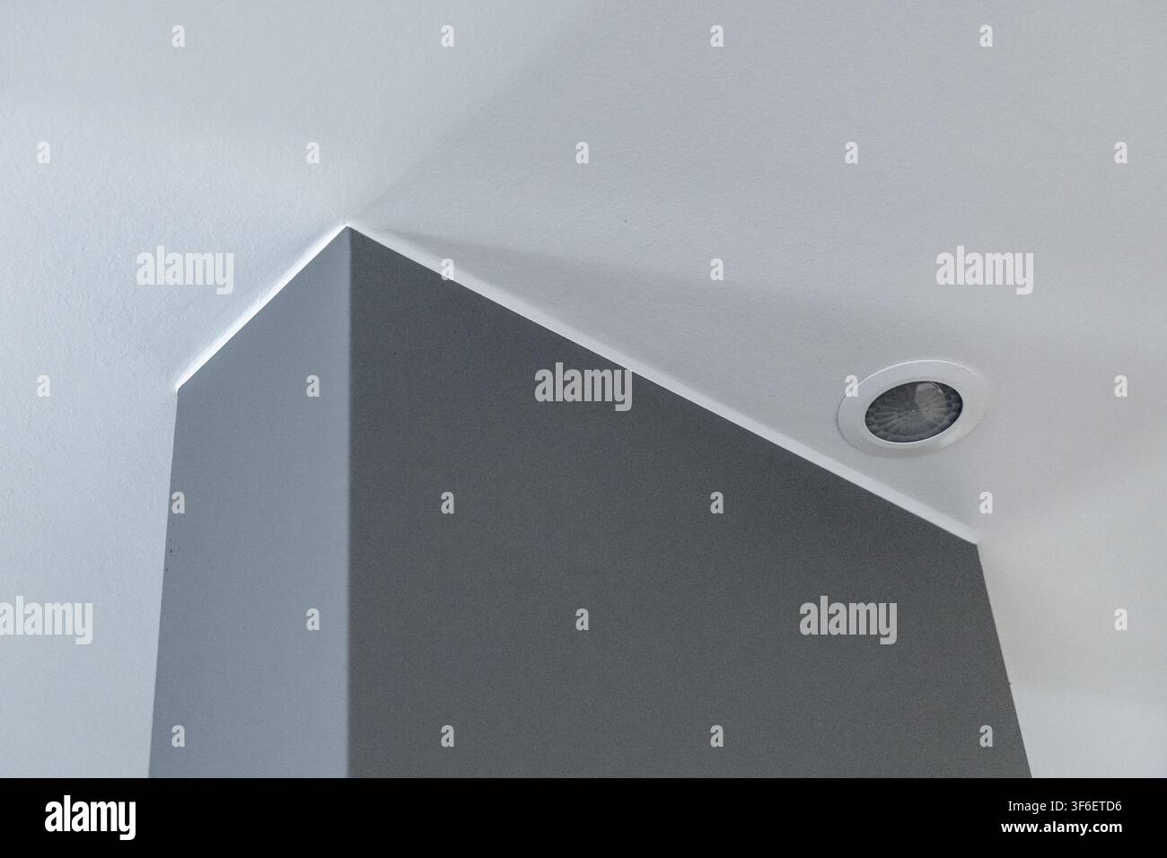 Abstract architectural detail featuring a sharp corner where a textured gray wall meets a white ceiling with a circular light fixture Stock Photo