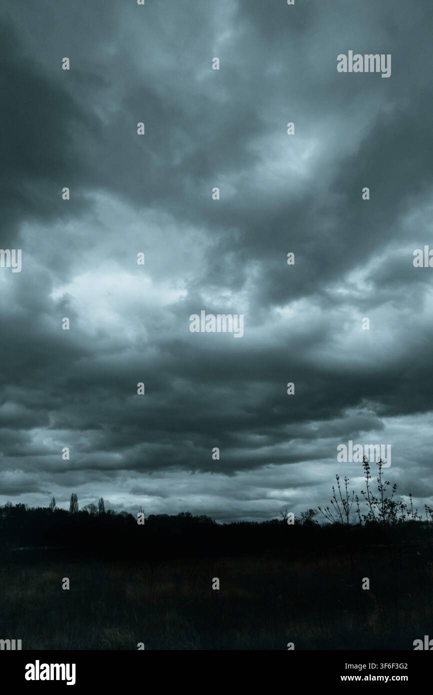 Dark storm clouds gather over a rural field and distant tree line, creating a dramatic, foreboding landscape before heavy rain Stock Photo