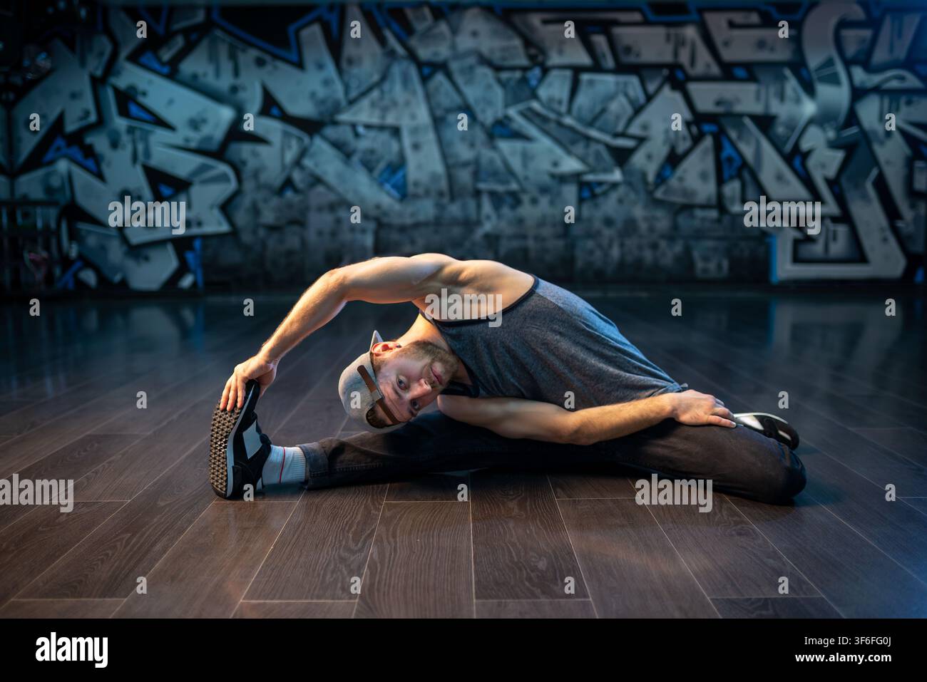 Bearded breakdancer in baseball cap doing wide leg stretch Stock Photo