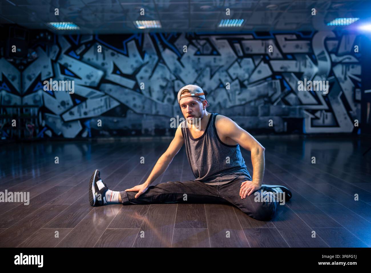 Bearded breakdancer in baseball cap doing wide leg stretch Stock Photo