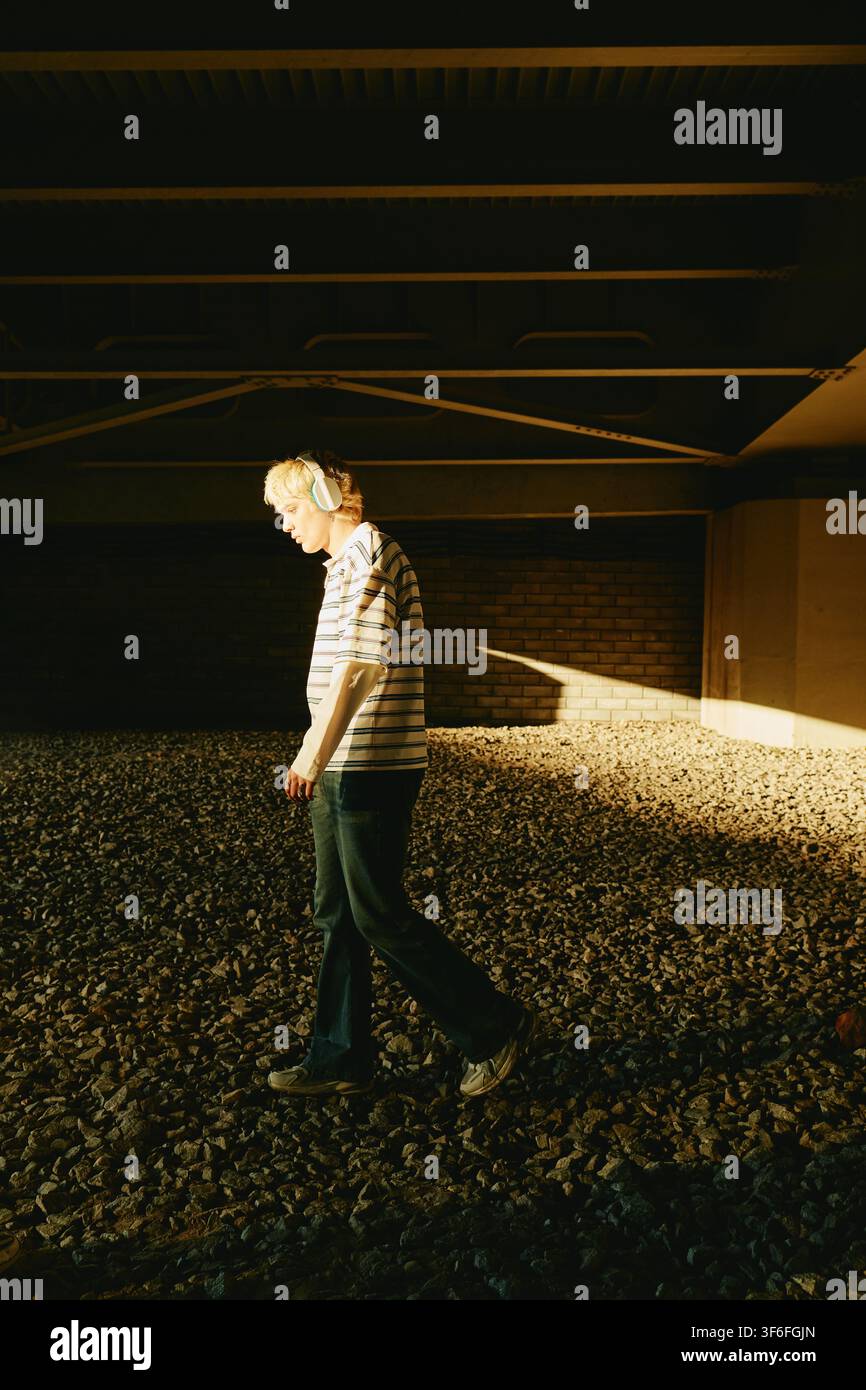 Man Wearing Headphones Walking Outdoors under Bridge Stock Photo