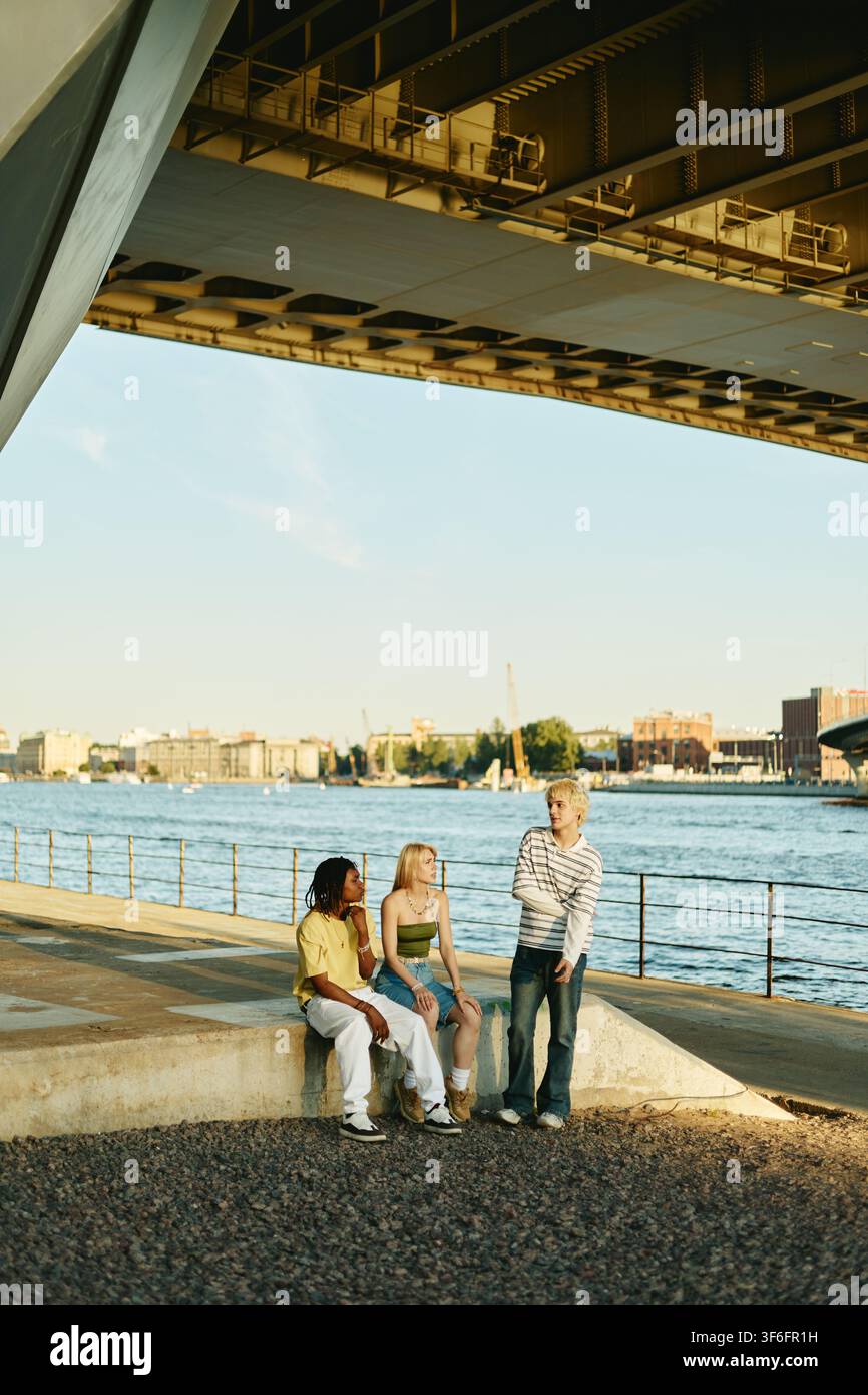 Diverse People Hanging out by River under Bridge Stock Photo