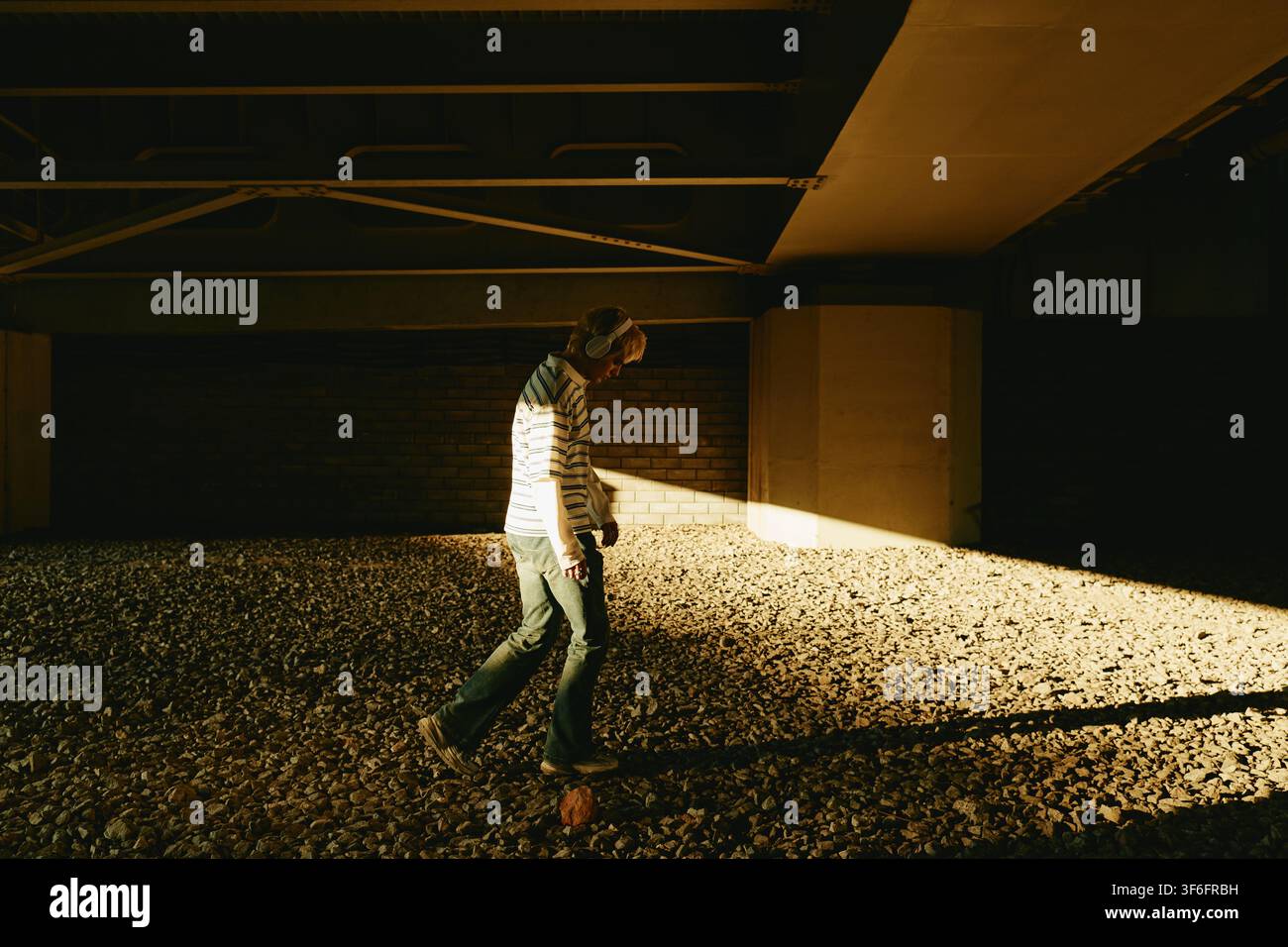 Man with Headphones Walking Outdoors under Bridge Stock Photo