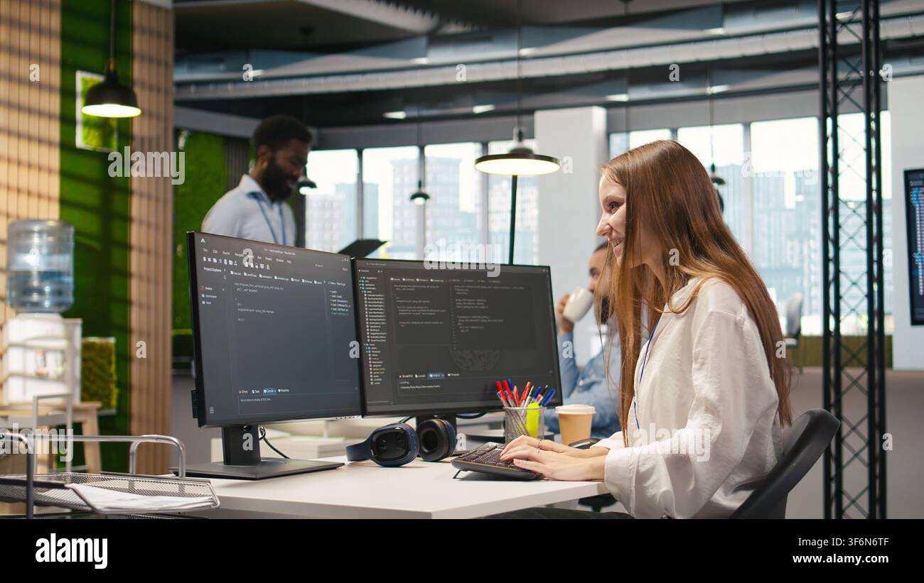 Young female programmer using computer to write code, developing machine learning APIs. Junior developer troubleshooting software errors and faults using artificial intelligence, camera A Stock Photo