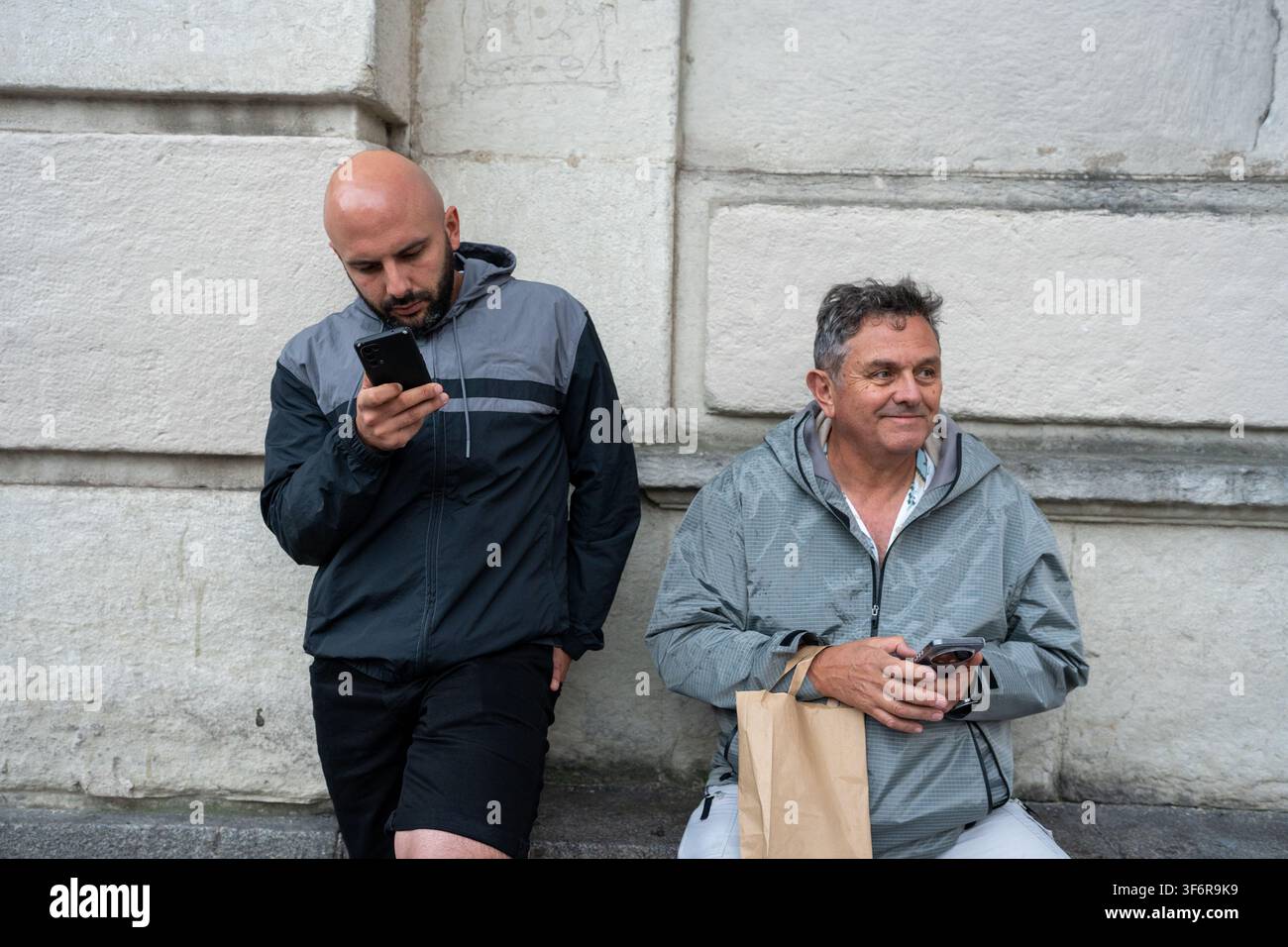 Two men waiting outdoors using smartphones Stock Photo