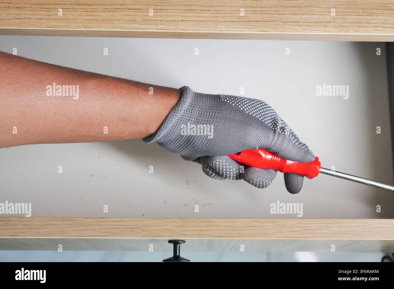 Person using screwdriver in kitchen cabinet Stock Photo