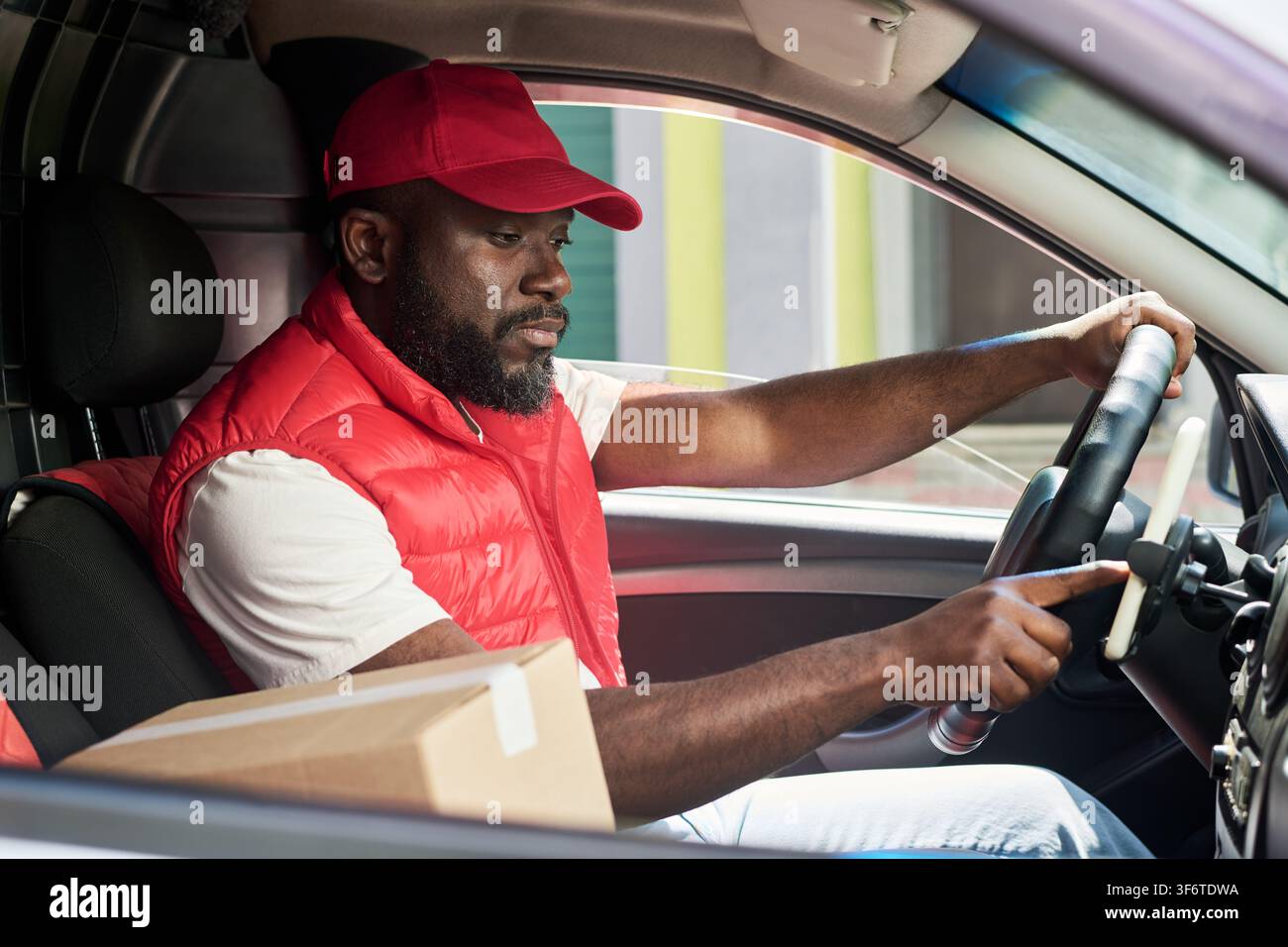 Black Courier Driving Delivery Van and Using Smartphone GPS Navigation Stock Photo