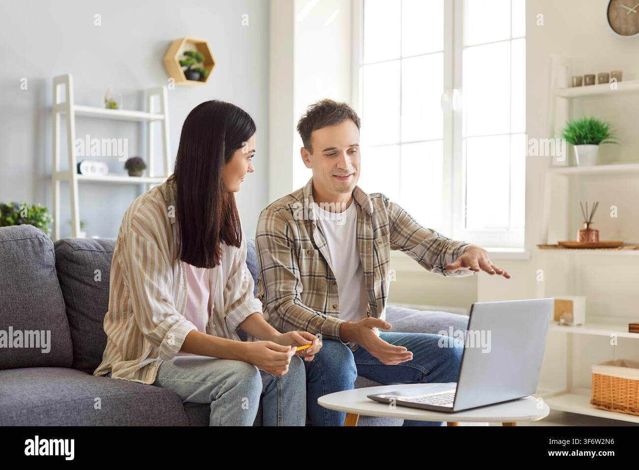 Couple sitting on sofa at home looking at laptop discussing ideas about interior design. Stock Photo