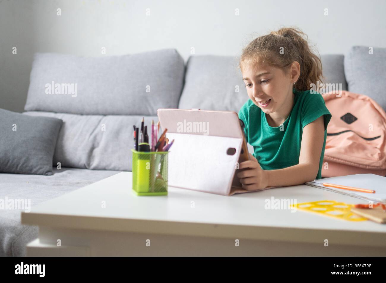 Happy elementary school girl smiling while using a digital tablet at home. Stock Photo