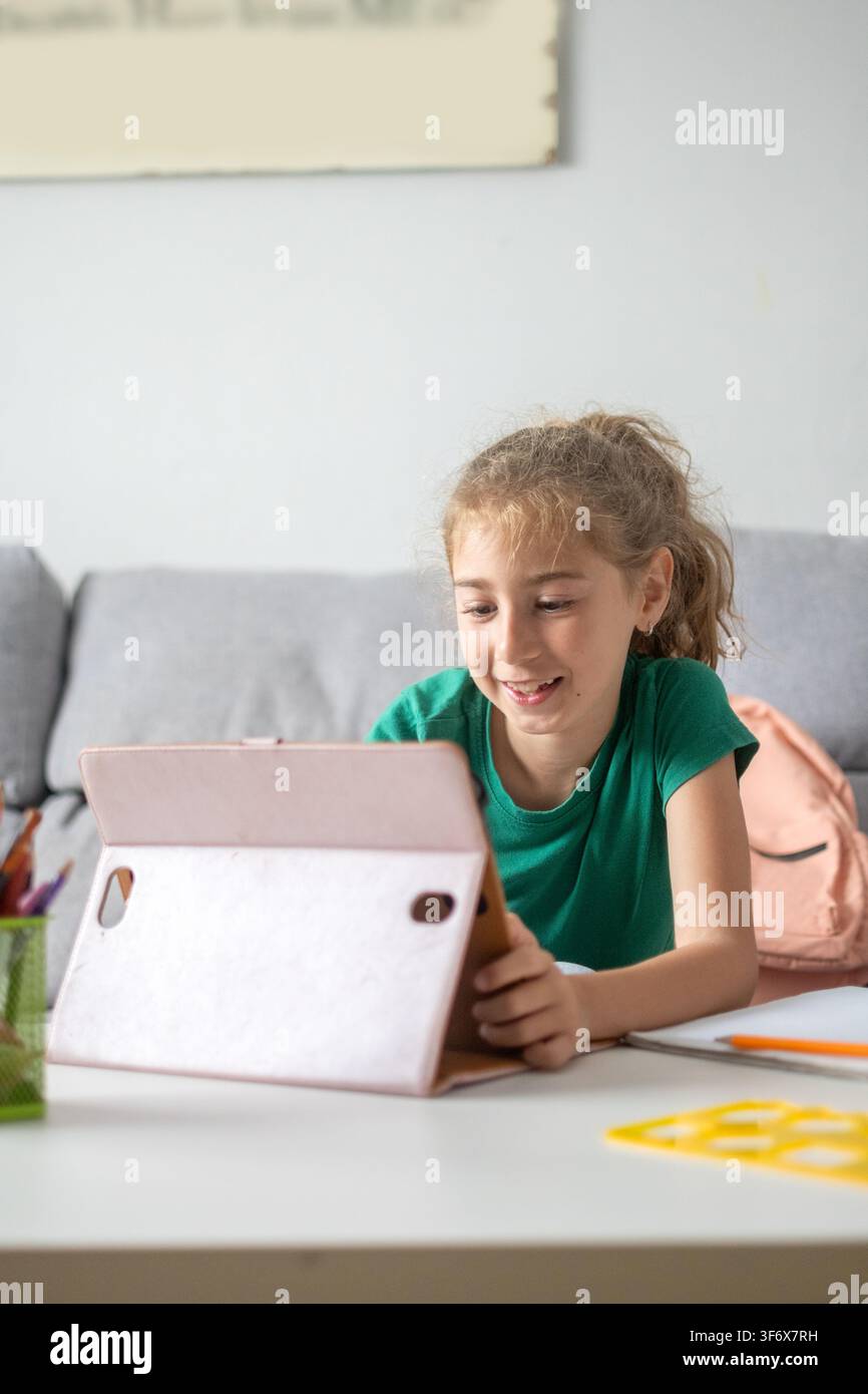 Happy elementary school girl smiling while using a digital tablet at home. Stock Photo