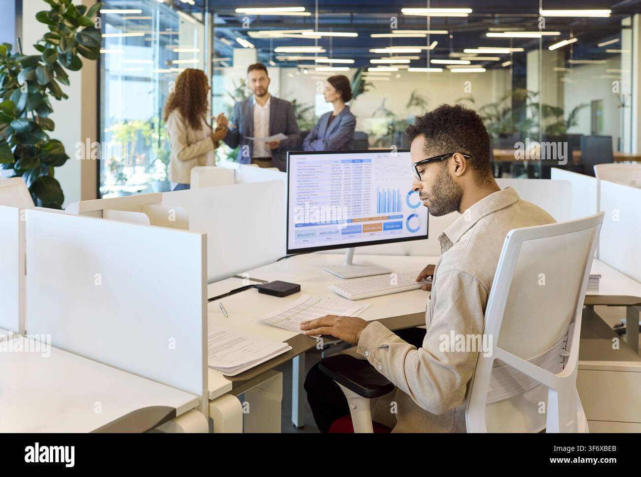 Young analyst working with financial spreadsheet at desktop in collaborative office Stock Photo