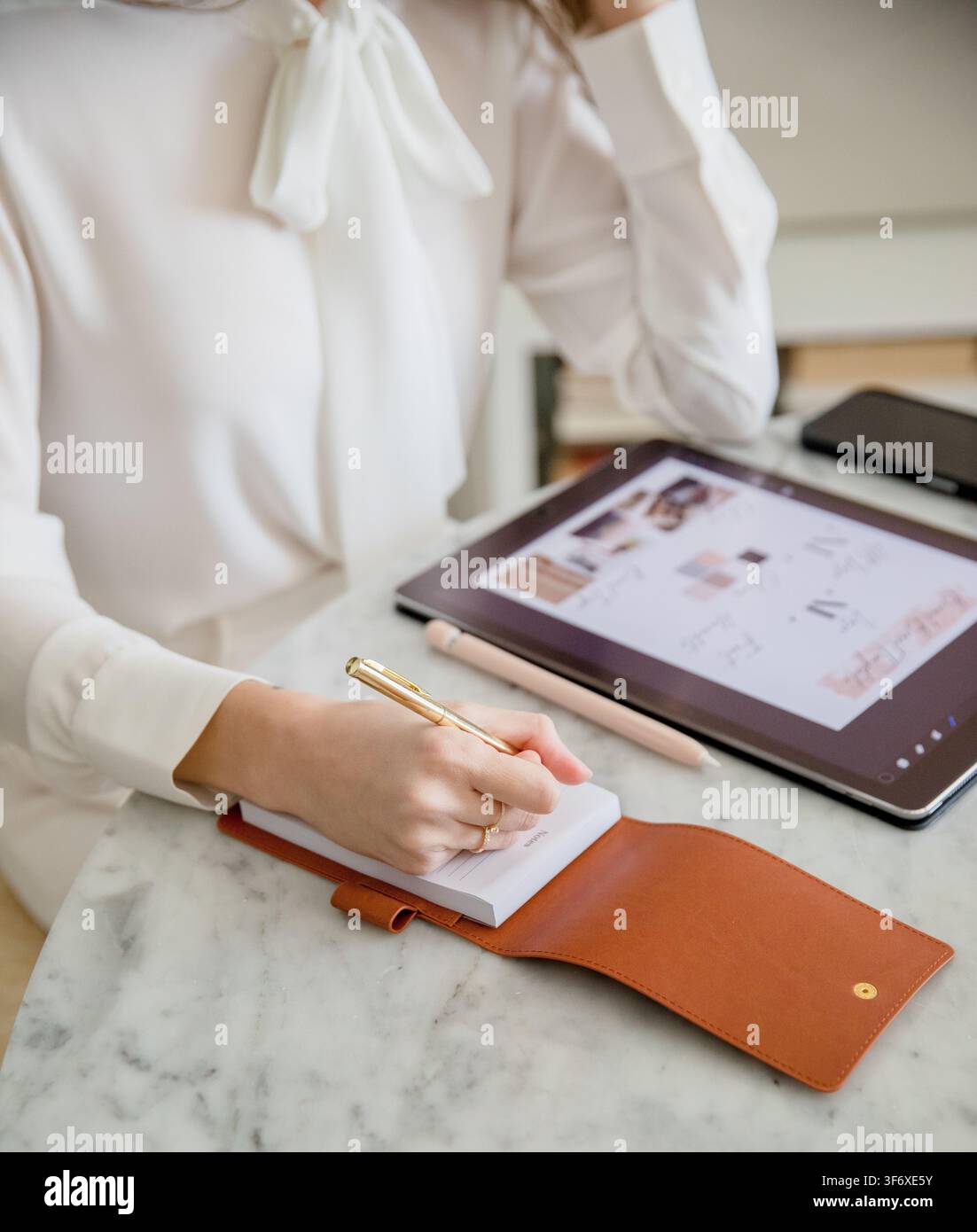 Woman Writing Notes on Notepad Beside Digital Tablet Stock Photo
