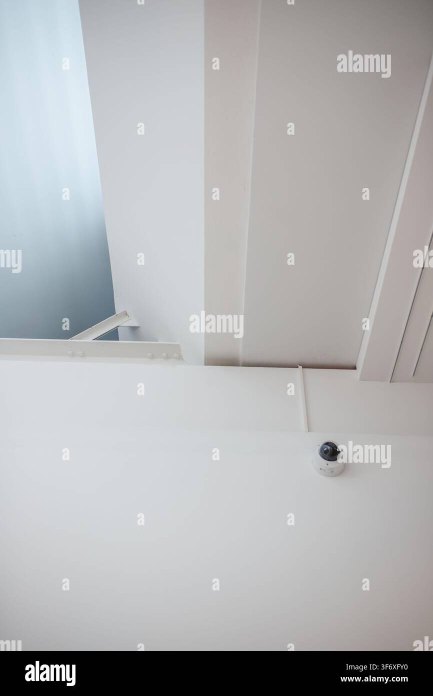 Security camera mounted on minimalist white ceiling architecture Stock Photo