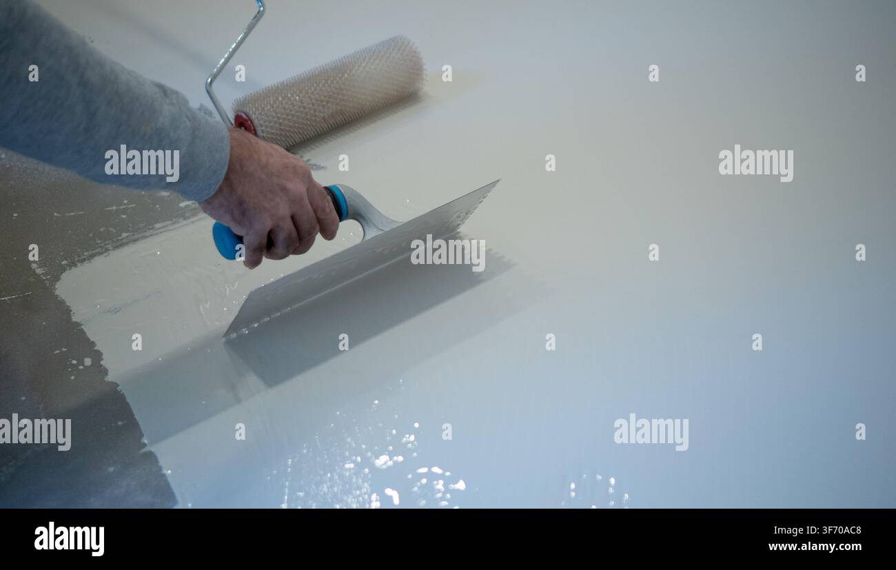 Worker Applying White Liquid Floor Coating With Roller and Trowel Stock Photo