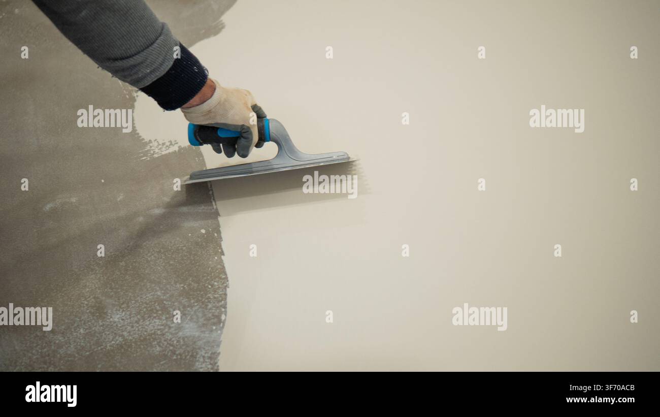 Worker Applying White Liquid Floor Coating With Roller and Trowel Stock Photo