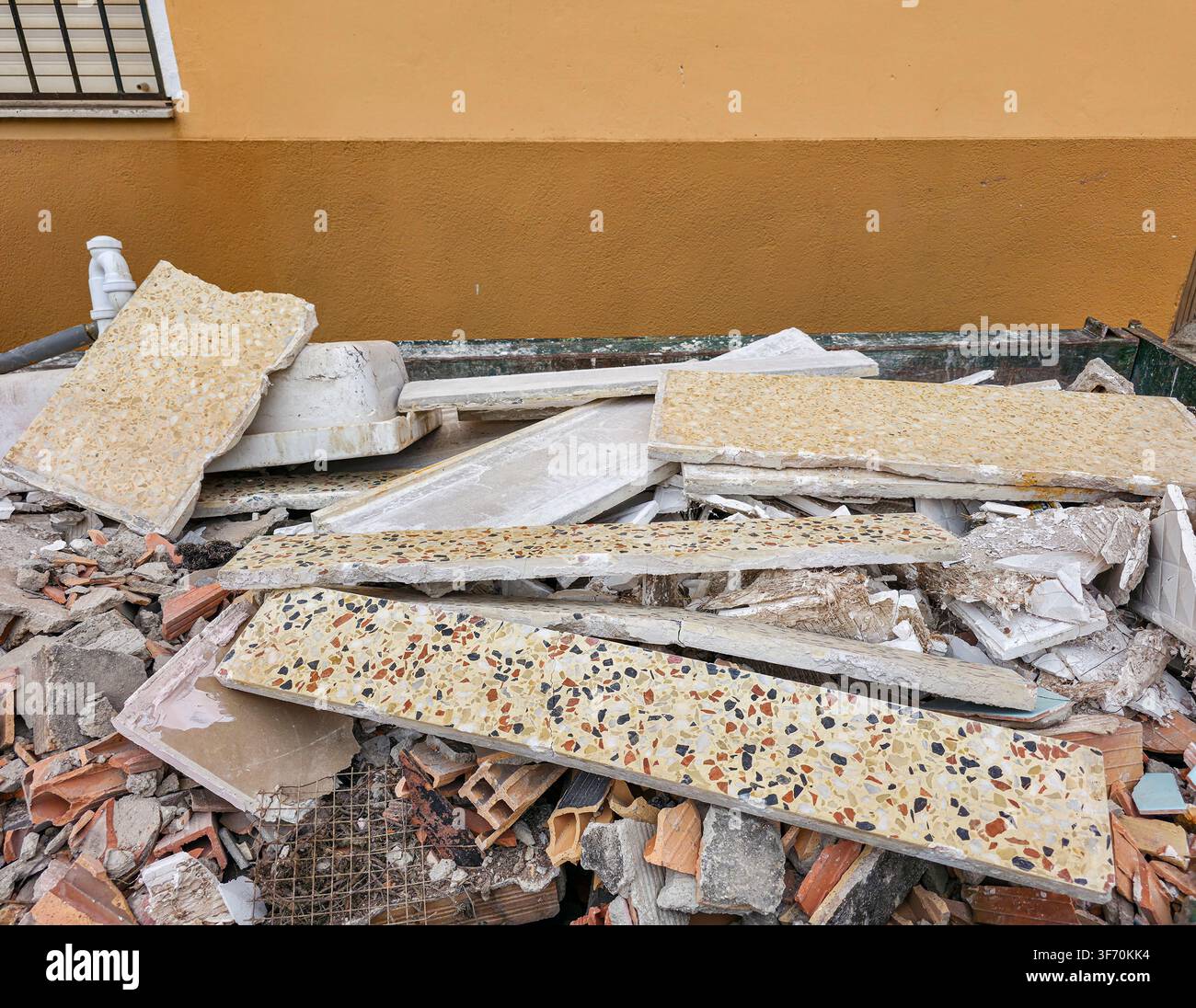 A container holds a mix of broken terrazzo tiles and concrete rubble from house renovation work in an outdoor setting. The area shows signs of ongoing Stock Photo