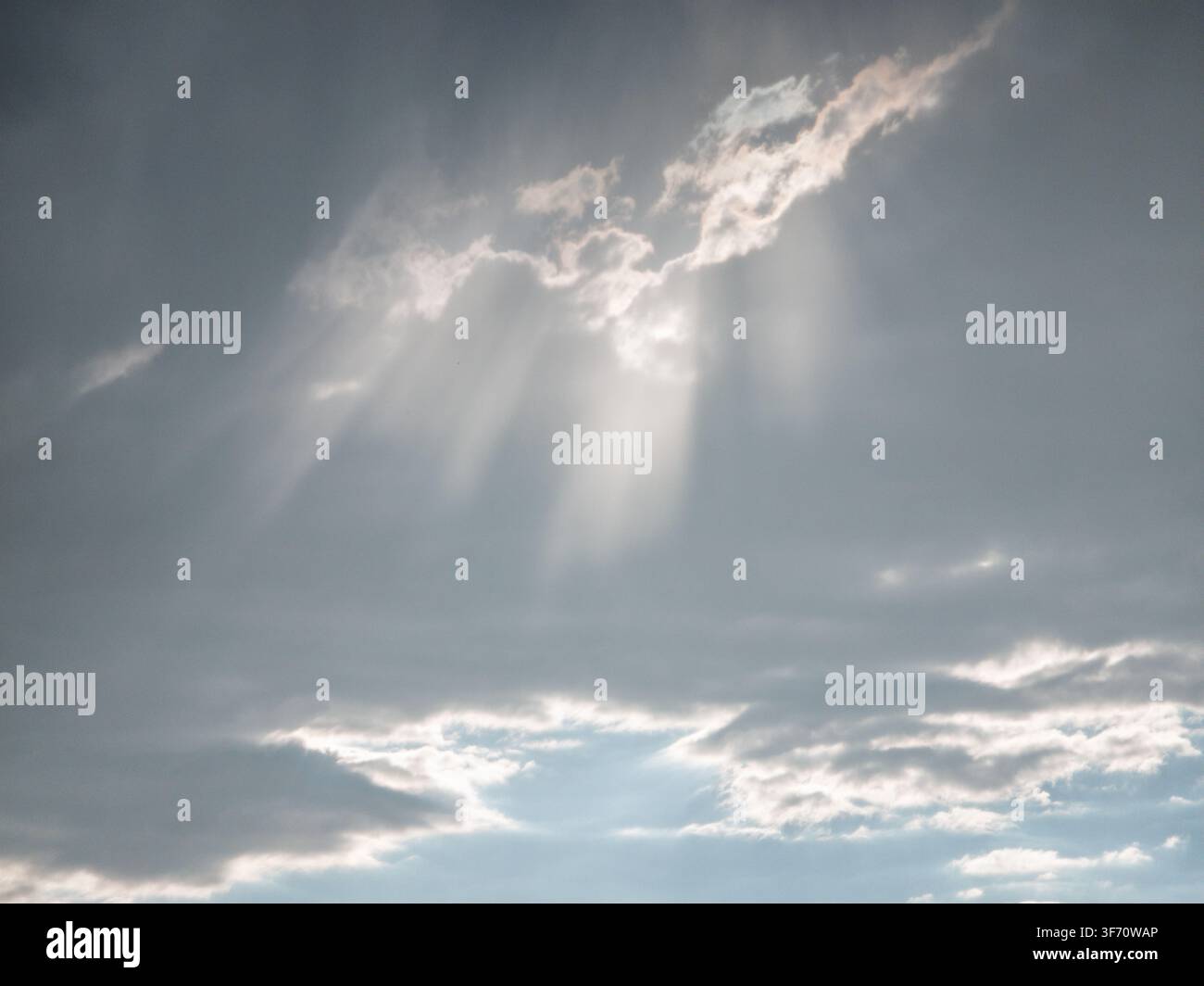 Sunlight breaks through gray clouds in dramatic rays. Sky scene with soft, diffused light filtering between cloud layers Stock Photo