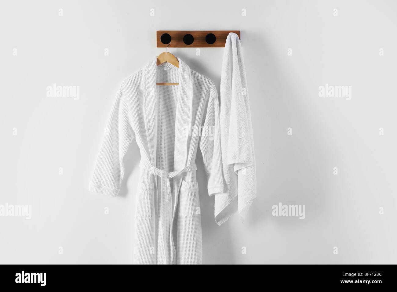 Clean cotton bathrobe and towel on white wall Stock Photo