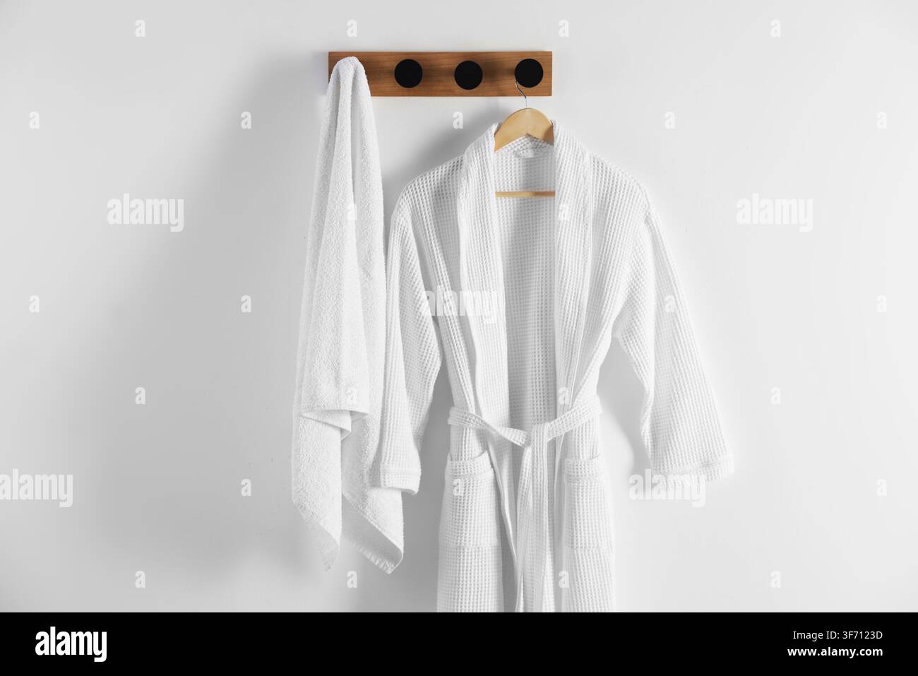 Clean cotton bathrobe and towel on white wall Stock Photo